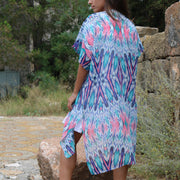 Woman wearing a colorful patterned short sleeve tunic standing outdoors with greenery in the background